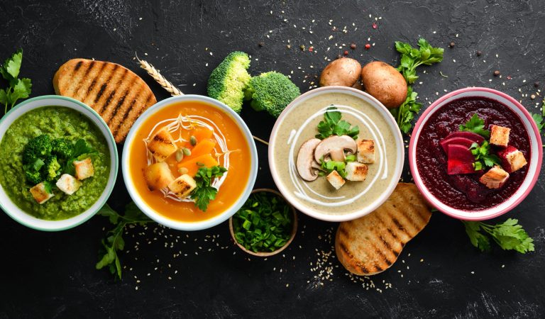 Assortment of colored vegetable cream soups. Dietary food. On a black stone background. Top view. Free copy space.